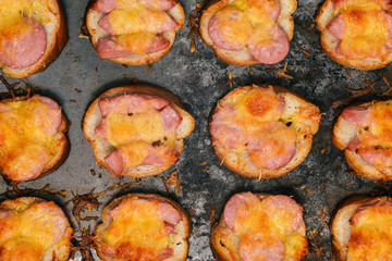 Melted cheese and fried sausages on bread. Baked sandwiches in a baking tray. Close-up of food. Appetizer for Breakfast, lunch, dinner or beer.