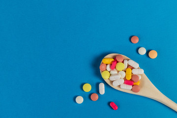 Mixed medicine pills, tablets on wooden spoon on blue background. Many different pills with space for text. Health care. Top view. Copy space. New image. Pharmaceutical picture. Good background