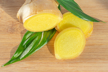Sliced ​​ginger root and green leaves on a wooden board. The concept of a healthy food, a cure for the common cold, flavoring. Close-up.