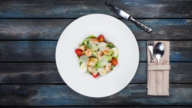 Fresh caesar salad rotating on white plate with parmesan cheese and shrimps. Is at a colored wooden background. Top view