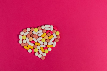 Many different pills and tablets folded in shape of heart on pink background. Many pills and tablets with space for text. Health care. Top view. Copy space. New image. Pharmaceutical picture