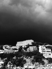 Moody black storm cloude over white hilltop hotel in Menorca