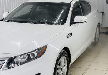 Fototapeta na wymiar Modern washing with foam and high-pressure water of a white car. Car wash