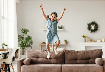 Happy girl listening to music and jumping on sofa.