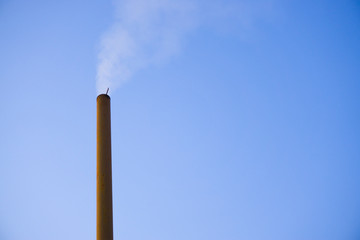 Steaming chimney smoke on isolated blue sky outdoor background. Climate change, environmental issue concept.
