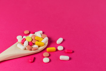Mixed medicine pills, tablets on wooden spoon on pink background. Different pills and tablets....