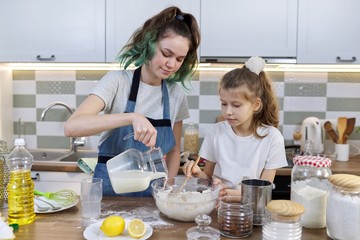 Obraz na płótnie Canvas Children two girls sisters preparing muffins in home kitchen, add milk to dough