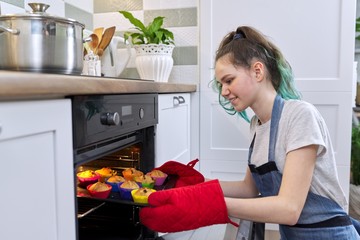 Girl taking cake with hot freshly baked muffins from the oven