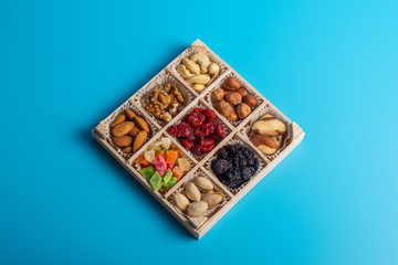 Assorted dried fruits and nuts in a wooden box isolated on a blue background. Raisins, candied fruits, cherries, Brazil nuts, hazelnuts, walnuts, almonds, cashews, pistachios.