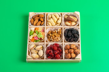 Assorted dried fruits and nuts in a wooden box isolated on a green background. Raisins, candied fruits, cherries, Brazil nuts, hazelnuts, walnuts, almonds, cashews, pistachios.