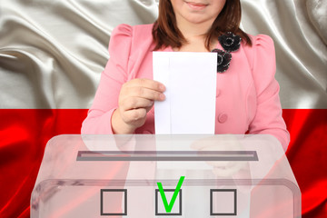 female voter drops a ballot in a transparent ballot box against the background of the national flag...