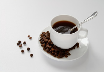 white cup with coffee, coffee seeds on a cup saucer and on a white table.