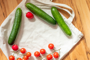 Small tomatoes, cucumbers and radishes on the cloth bag lie in a circle.