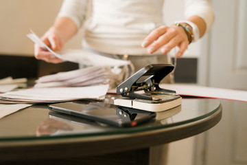 close up on hole puncher on the table at the office in day front view with unknown woman caucasian female standing behind working with documents holding paper