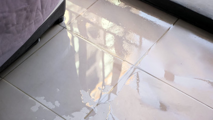 trembling water puddle after pipe burst covers white tile near furniture in room reflecting window...