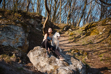 Sporty young woman with her dog samoyed sitting on a stone in the park and enjoys a sunny spring day. Running with dog, spring time
