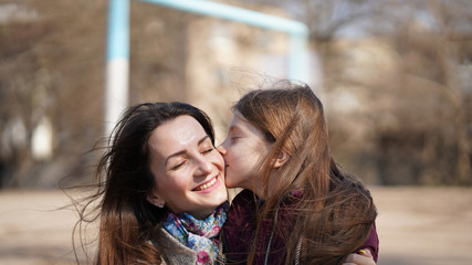 Obraz premium Cute pretty daughter kiss her beautiful Mom on playground