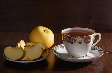 Cup of tea and plate with apples on dark background with opposite light
