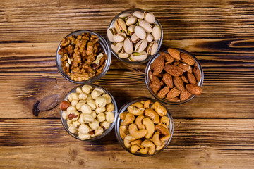 Various nuts (almond, cashew, hazelnut, pistachio, walnut) in glass bowls on a wooden table. Vegetarian meal. Healthy eating concept. Top view