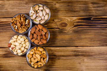 Various nuts (almond, cashew, hazelnut, pistachio, walnut) in glass bowls on a wooden table. Vegetarian meal. Healthy eating concept. Top view