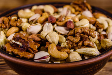 Various nuts (almond, cashew, hazelnut, pistachio, walnut) in ceramic plate on a wooden table. Vegetarian meal. Healthy eating concept