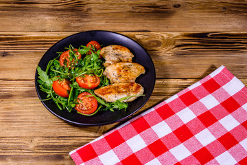 Roasted chicken breasts and salad with arugula and cherry tomatoes in a black plate