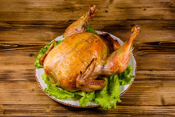 Plate with roasted whole chicken and lettuce leaves on a wooden table