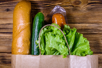 Paper bag with different food from grocery on a wooden table. Supermarket shopping concept. Top view