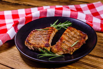 Plate with roasted steaks and rosemary twigs on a wooden table