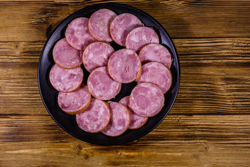 Black plate with sliced sausage on a wooden table. Top view