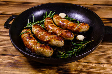 Roasted sausages with rosemary twigs and garlic in a cast iron grill pan