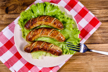 Plate with roasted sausages and lettuce leaves on a wooden table