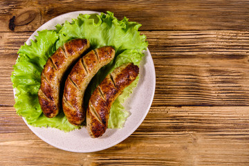 Plate with roasted sausages and lettuce leaves on a wooden table. Top view