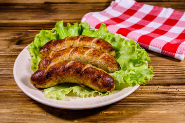 Plate with roasted sausages and lettuce leaves on a wooden table