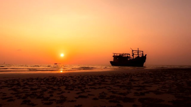 Sunset at the colourful seashore behind the boat in Thailand. Timelapse of the sun that goes down at the seashore while other people walk there. Concept of travelling and vacation near the ocean.