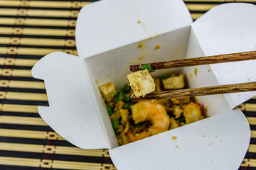 Naklejka na ściany i meble Paper box with pad thai on a bamboo mat. Chopsticks with tofu