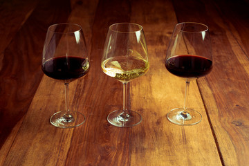 tres copas de vino tinto y vino blanco sobre una mesa de madera 