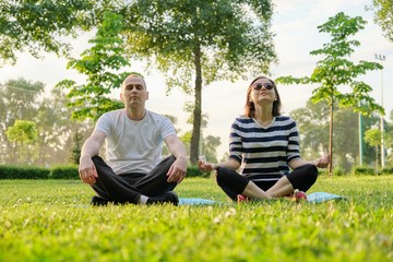 Couple, man and woman sitting in park on mat in lotus position and meditating