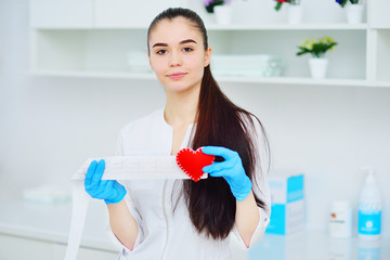 a woman doctor holds a red heart and a paper printout of a cardiogram. Prevention of cardiovascular...