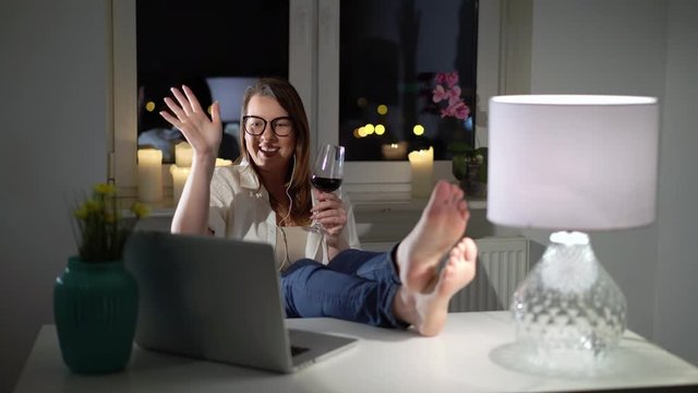 Young woman working at computer laptop at home evening with wine, video call