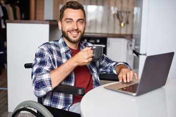 Young handsome man in wheelchair working on laptop at home