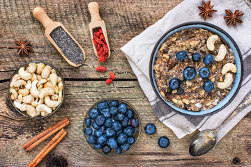 Bowl of oatmeal porridge with banana, blueberries, cashew, coconut, goji berries and with bananas on rustic table, hot and healthy food for breakfast.