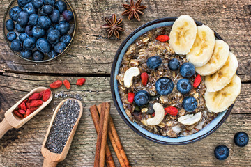 Bowl of oatmeal porridge with banana, blueberries, cashew, coconut, goji berries and with bananas on rustic table, hot and healthy food for breakfast.