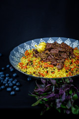 Pilaf and ingredients on plate with oriental ornament on a black background. Central-Asian cuisine - Plov Top view