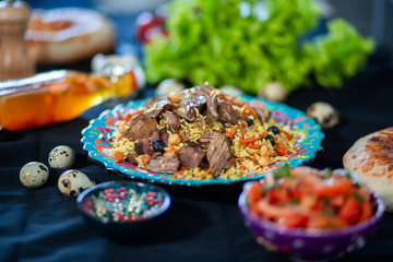 Pilaf and ingredients on plate with oriental ornament on a black background. Central-Asian cuisine - Plov Top view