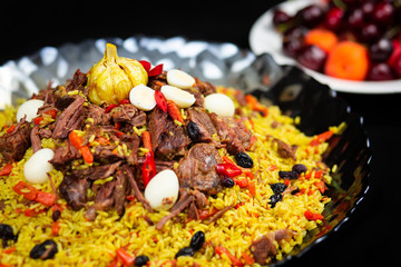 Pilaf and ingredients on plate with oriental ornament on a black background. Central-Asian cuisine - Plov Top view