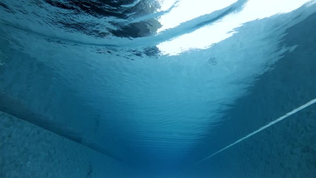 Young man in swimsuit swims one way in the waterpool freestyle. Slow motion of the swimmer making waves and splashes and moving his hands. Concept of healthy activities on vacations.