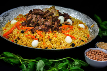 Pilaf and ingredients on plate with oriental ornament on a black background. Central-Asian cuisine - Plov Top view