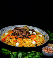 Pilaf and ingredients on plate with oriental ornament on a black background. Central-Asian cuisine - Plov Top view