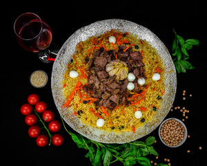 Pilaf and ingredients on plate with oriental ornament on a black background. Central-Asian cuisine - Plov Top view